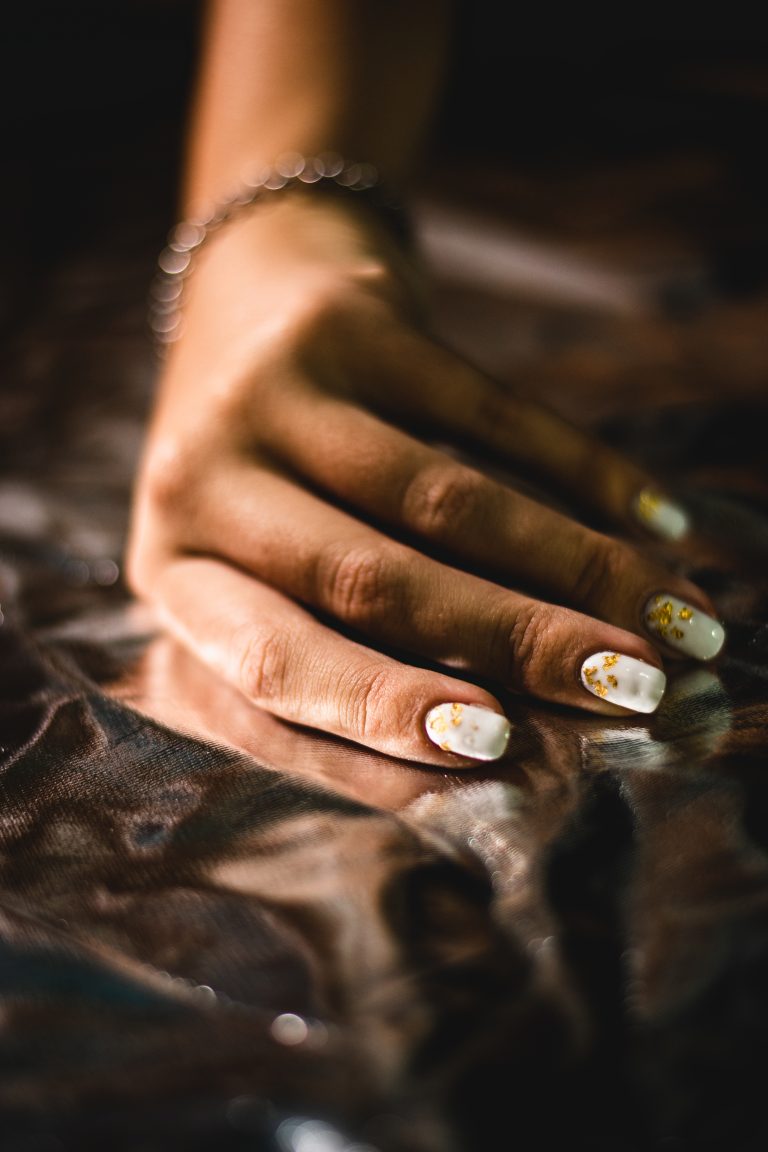 A vertical closeup of the woman's hand with white manicure.